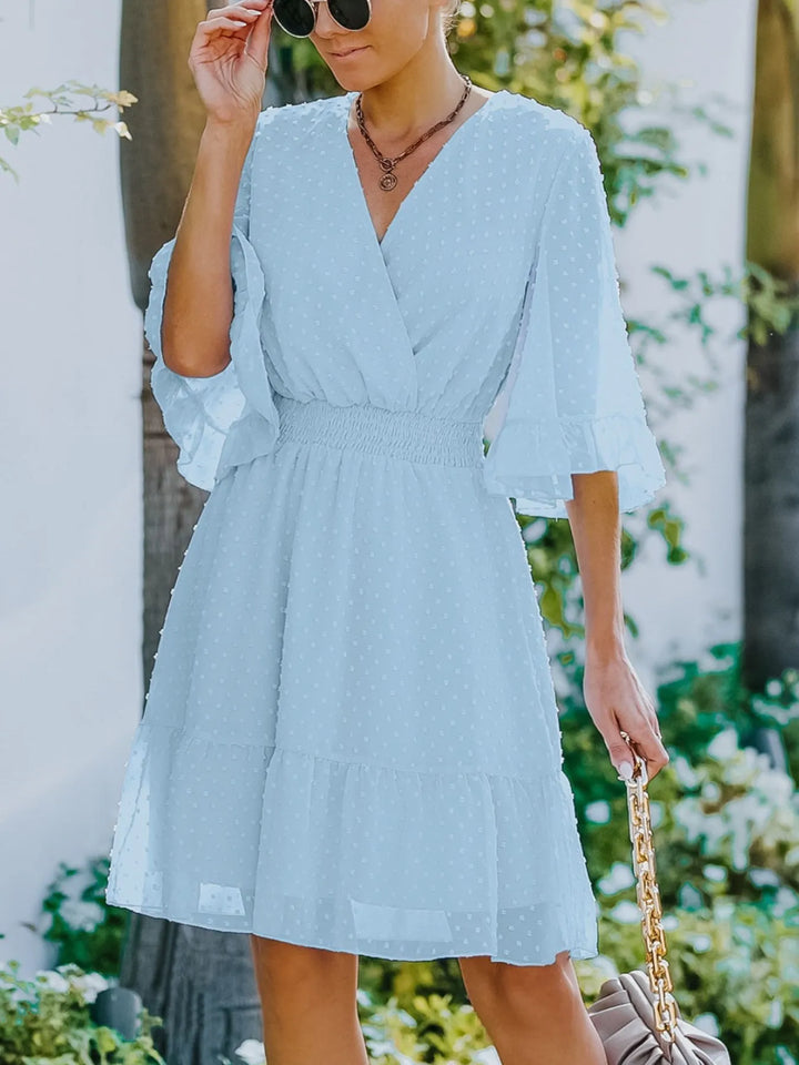 Woman wearing a light blue dress with ruffled sleeves in an outdoor setting.