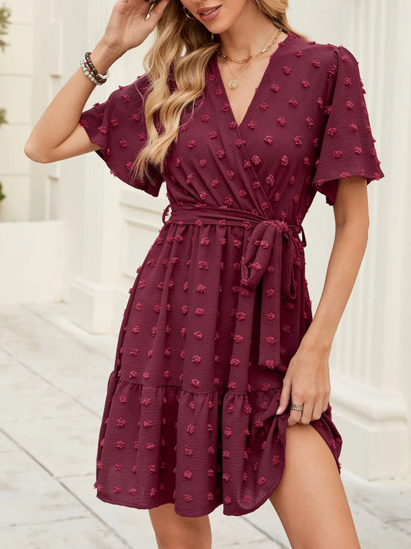 Woman wearing a burgundy swiss dot dress with a pattern, standing against a light background