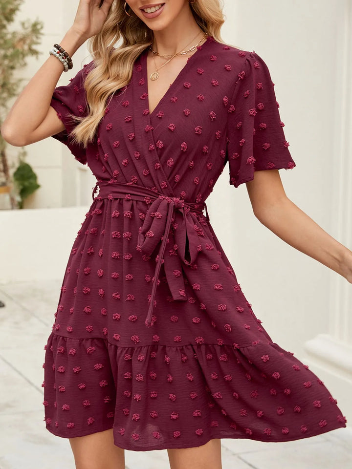 Woman wearing a burgundy Swiss Dot dress with floral patterns against a neutral background