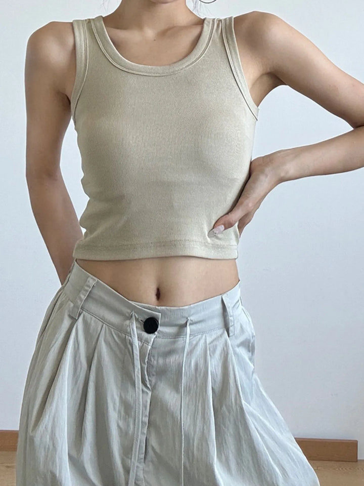 Person wearing a beige tank cropped top and light-colored pants against a plain background