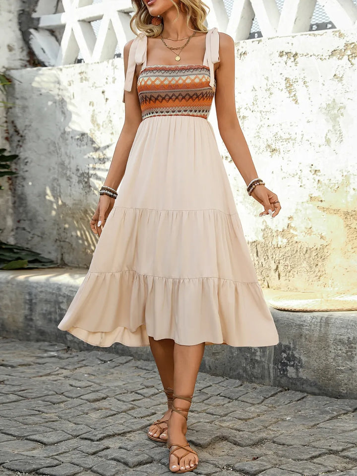 Woman wearing a beige dress with a patterned bodice standing on a stone path.