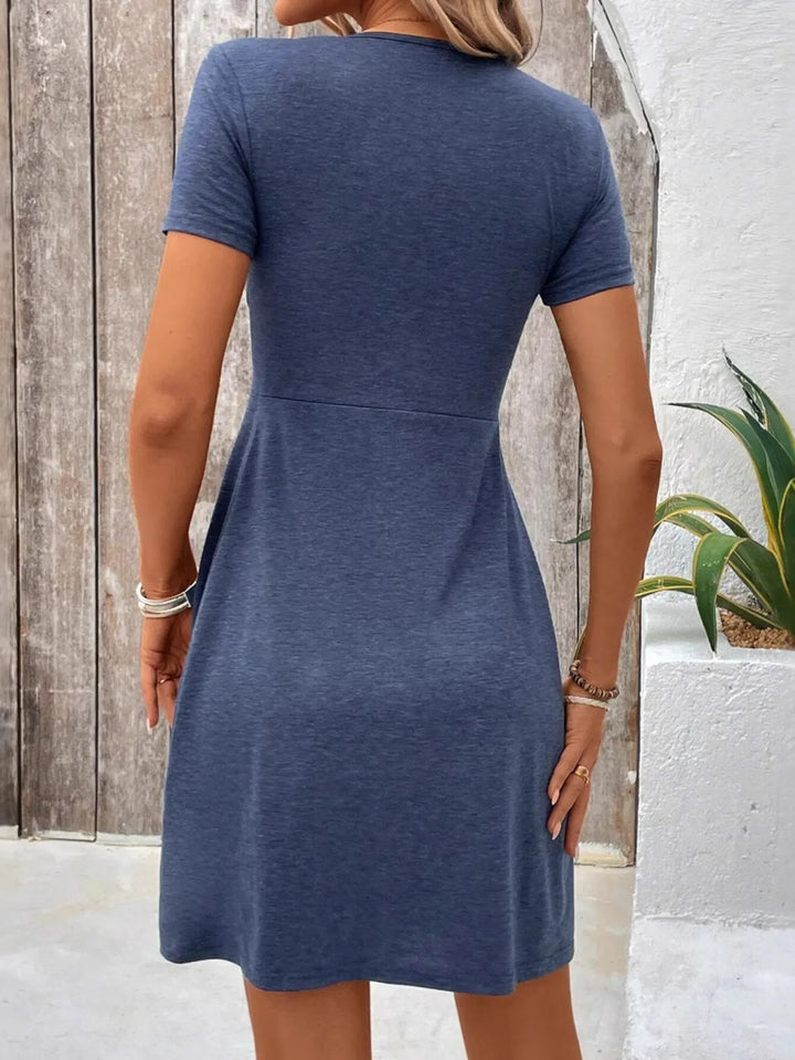 Woman wearing a blue casual dress standing against a wooden and white wall.