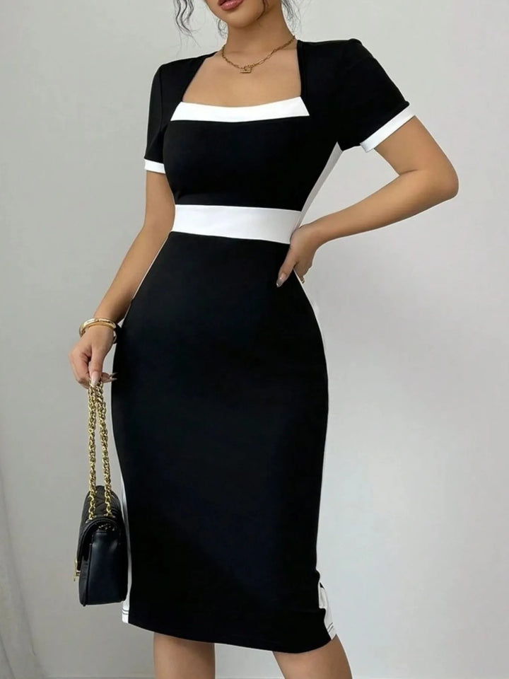 Woman wearing a black and white midi dress holding a handbag against a plain background