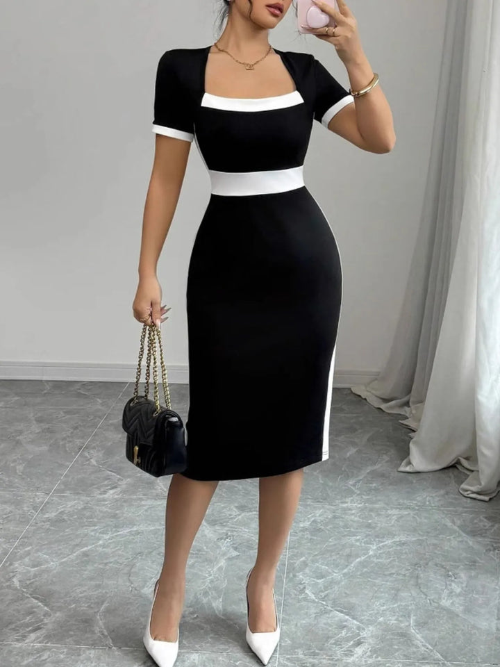 Woman wearing a black and white midi dress holding a handbag indoors.
