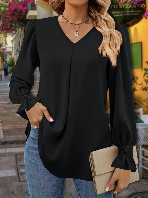 Woman wearing a black blouse with long sleeves and blue jeans, holding a beige clutch.