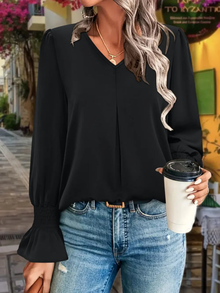 Woman wearing a black blouse and blue jeans, holding a coffee cup outdoors.