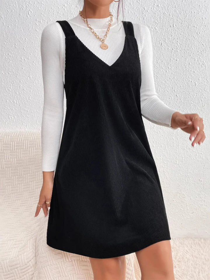 Person wearing a black casual sleeveless dress over a white long-sleeve shirt against a light background