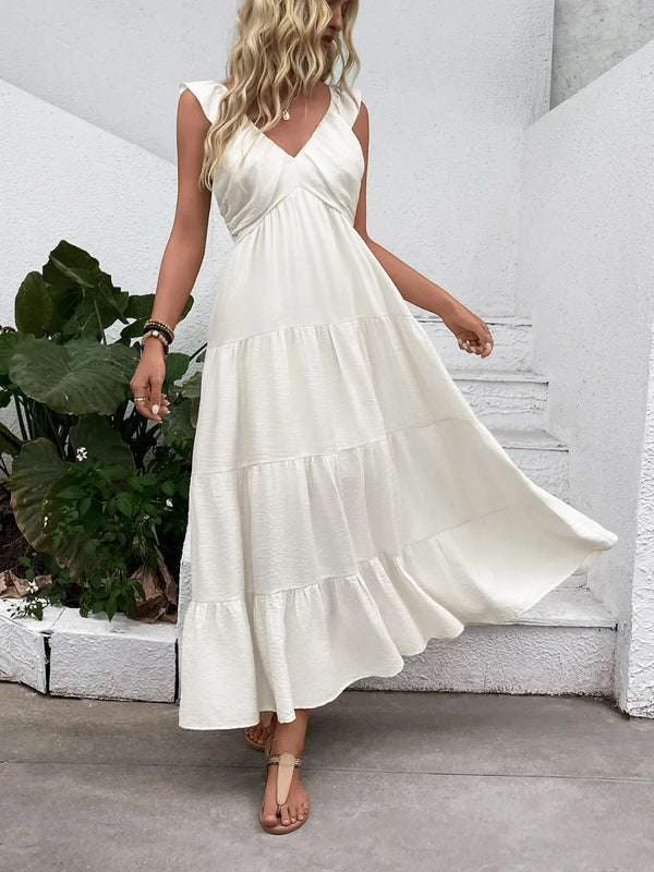 Woman wearing a white tiered dress standing in front of a white wall with plants.