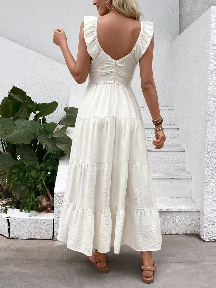 Woman wearing a white dress with an open back, standing outdoors.