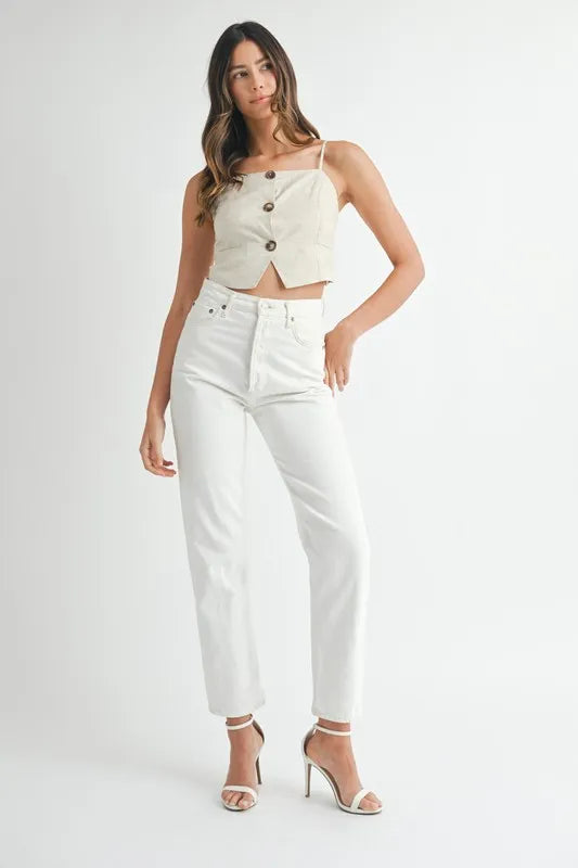 Woman wearing a white sleeveless top with cut-out design and high-waisted white pants on a white background