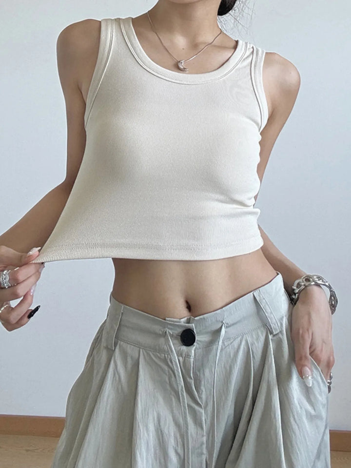 Person wearing a beige tank top and light-colored pants against a plain background