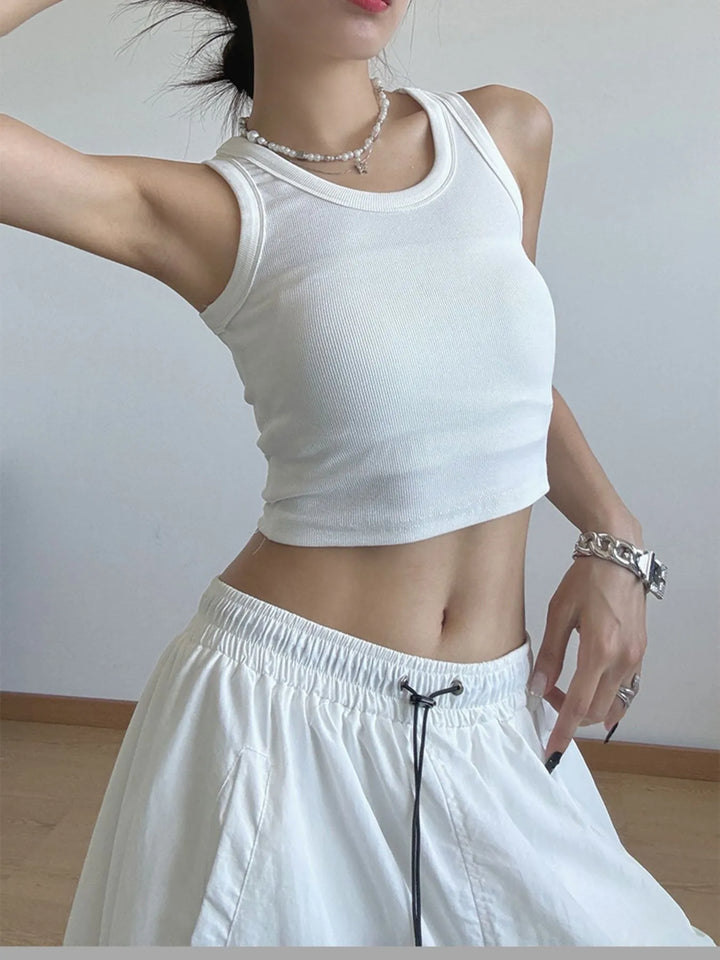 Person wearing a white sleeveless top and light-colored pants against a plain background