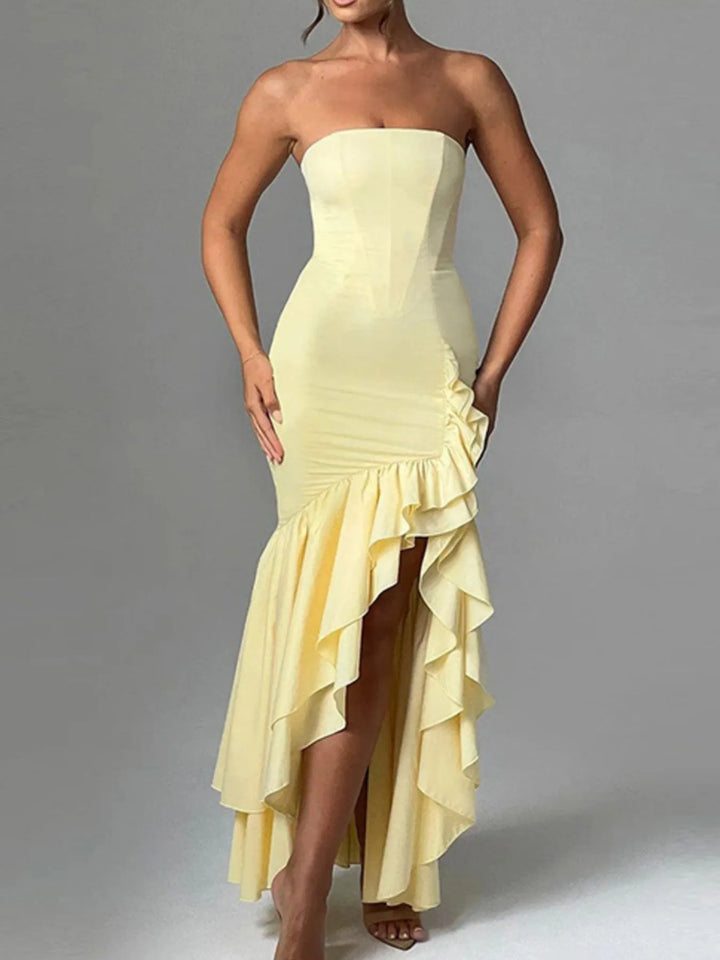 Woman wearing a strapless yellow evening gown with ruffled skirt on a gray background